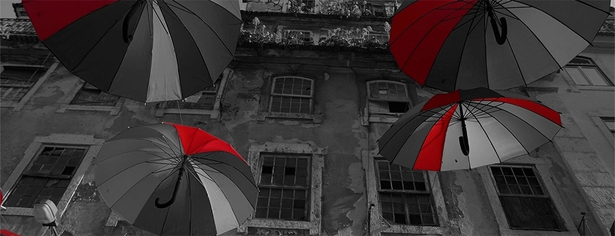 Guarda-chuvas em preto e vermelho, inspirados na instalação de Joana Vasconcelos, flutuam sobre uma rua antiga – uma metáfora visual para a criatividade e diferenciação da nossa agência de marketing digital.